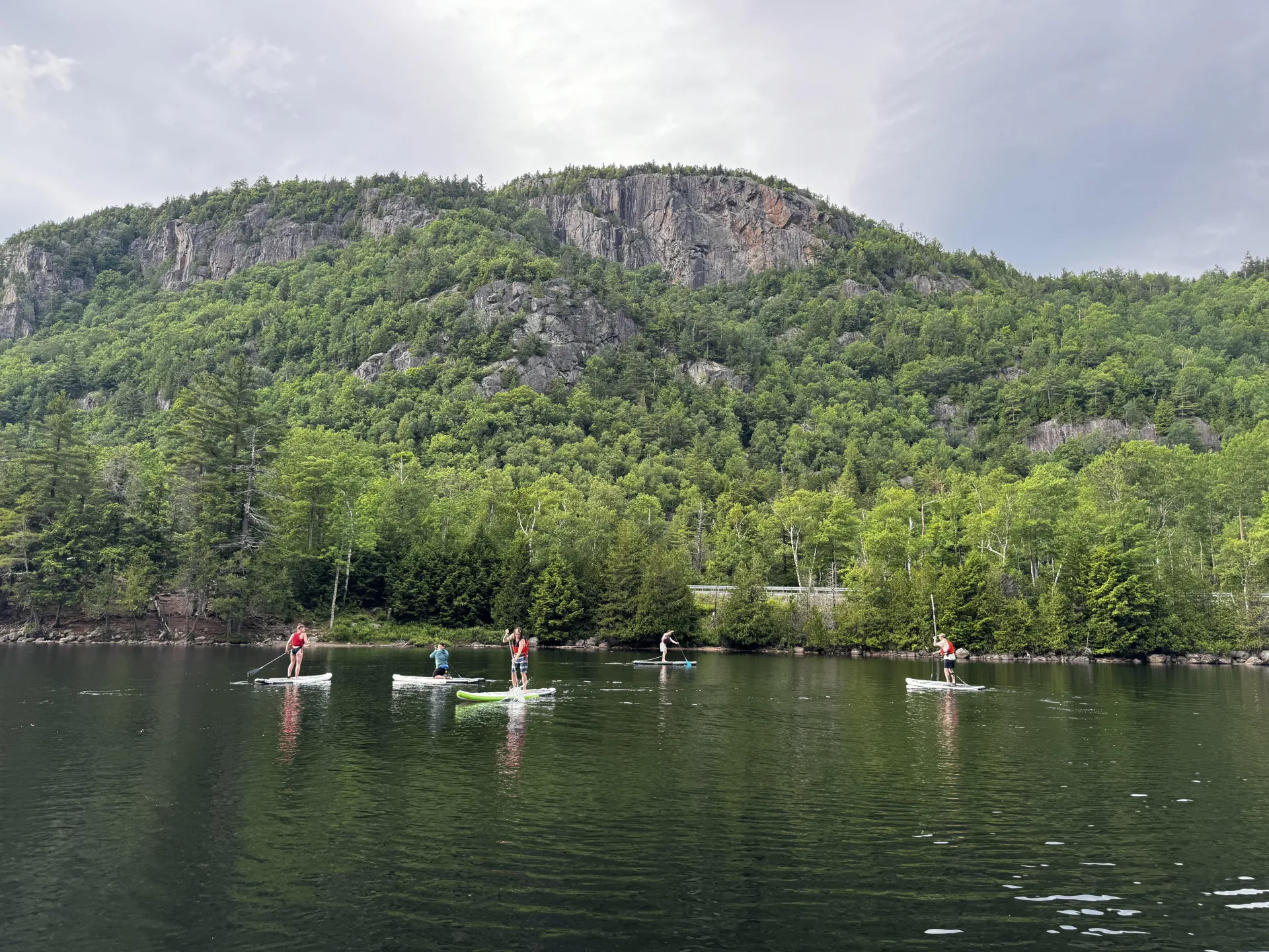 Five people are seen paddling on NRS paddle boards during a paddle clinic on Chapel Pond in the Adirondacks