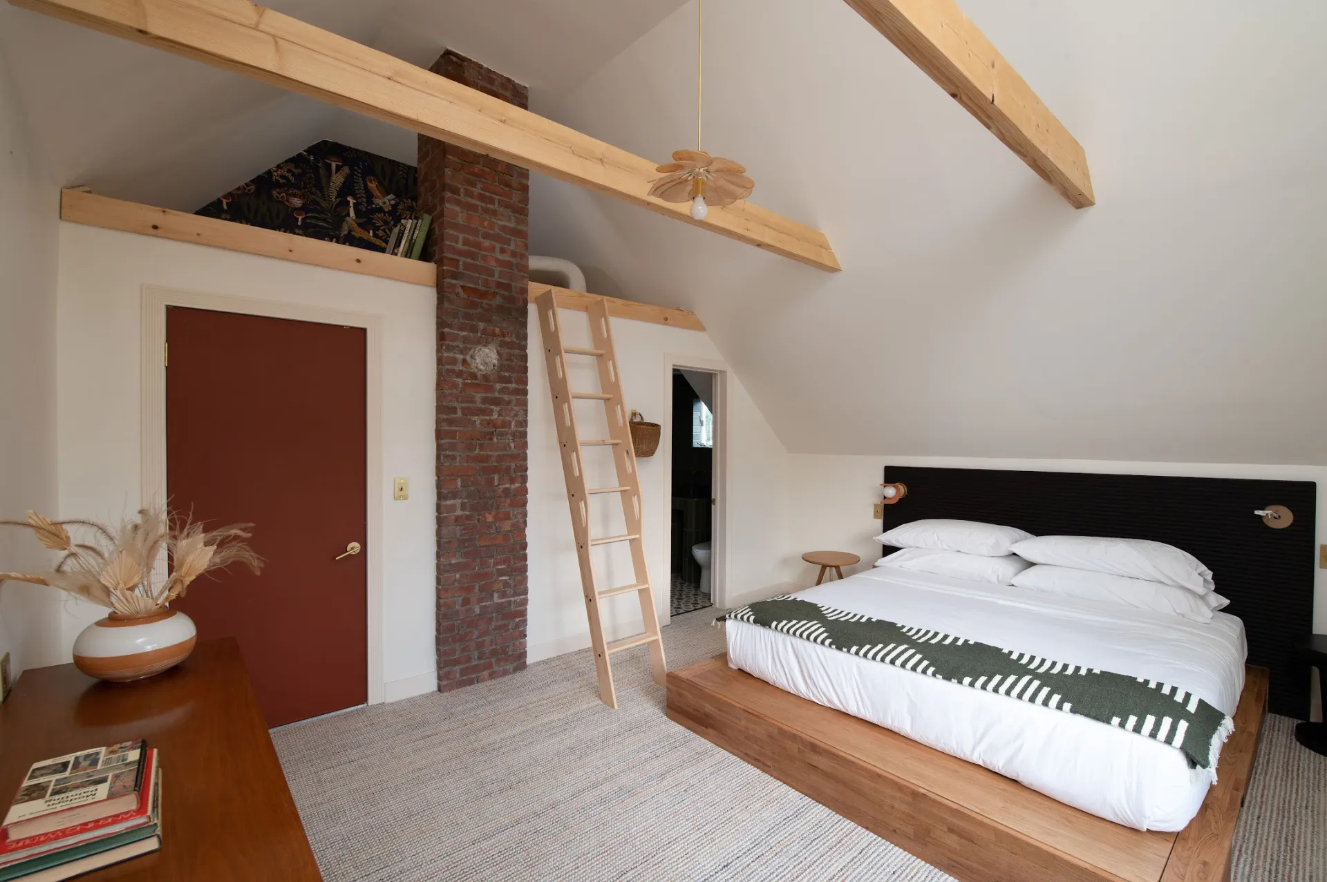 A sleeping space with wooden platform bed, and unique reading loft behind a brick chimney.