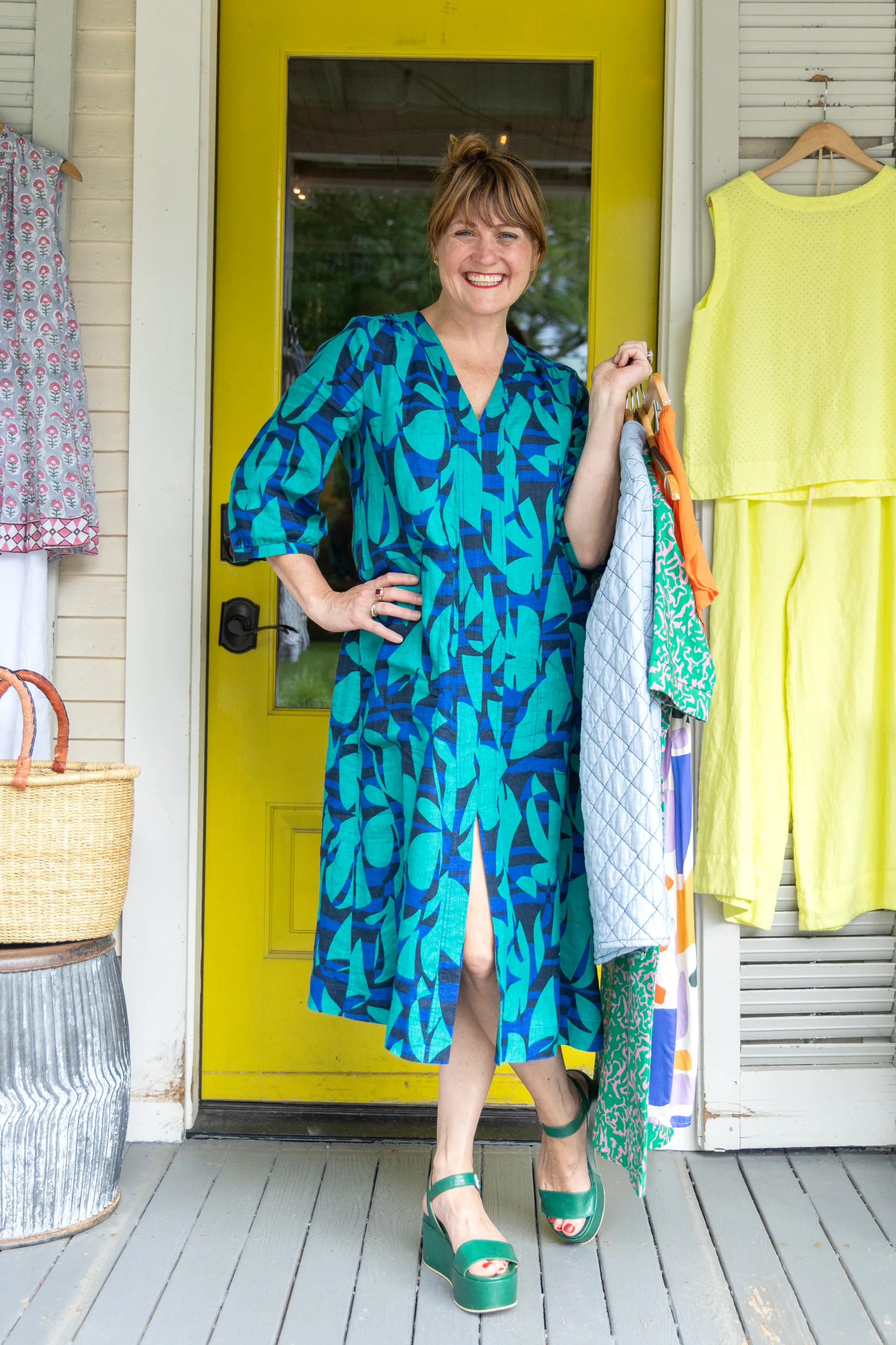 A happy lady in her blue dress stands holding her clothing haul.