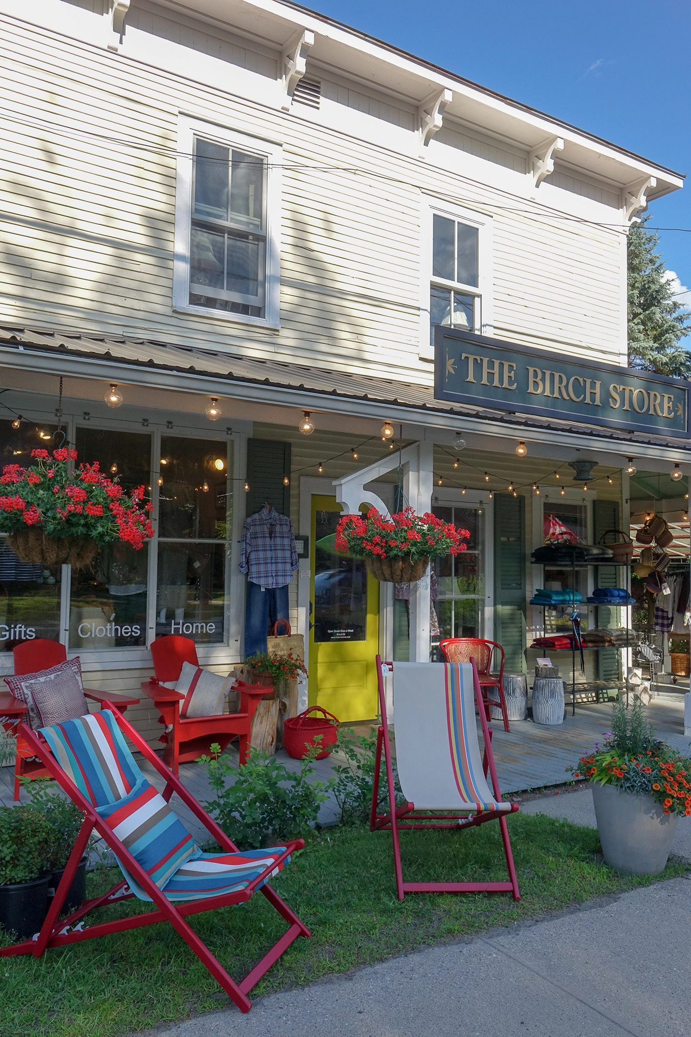 The exterior of The Birch Store decorated for the summer season with brightly colored lawn chairs and hanging flower baskets