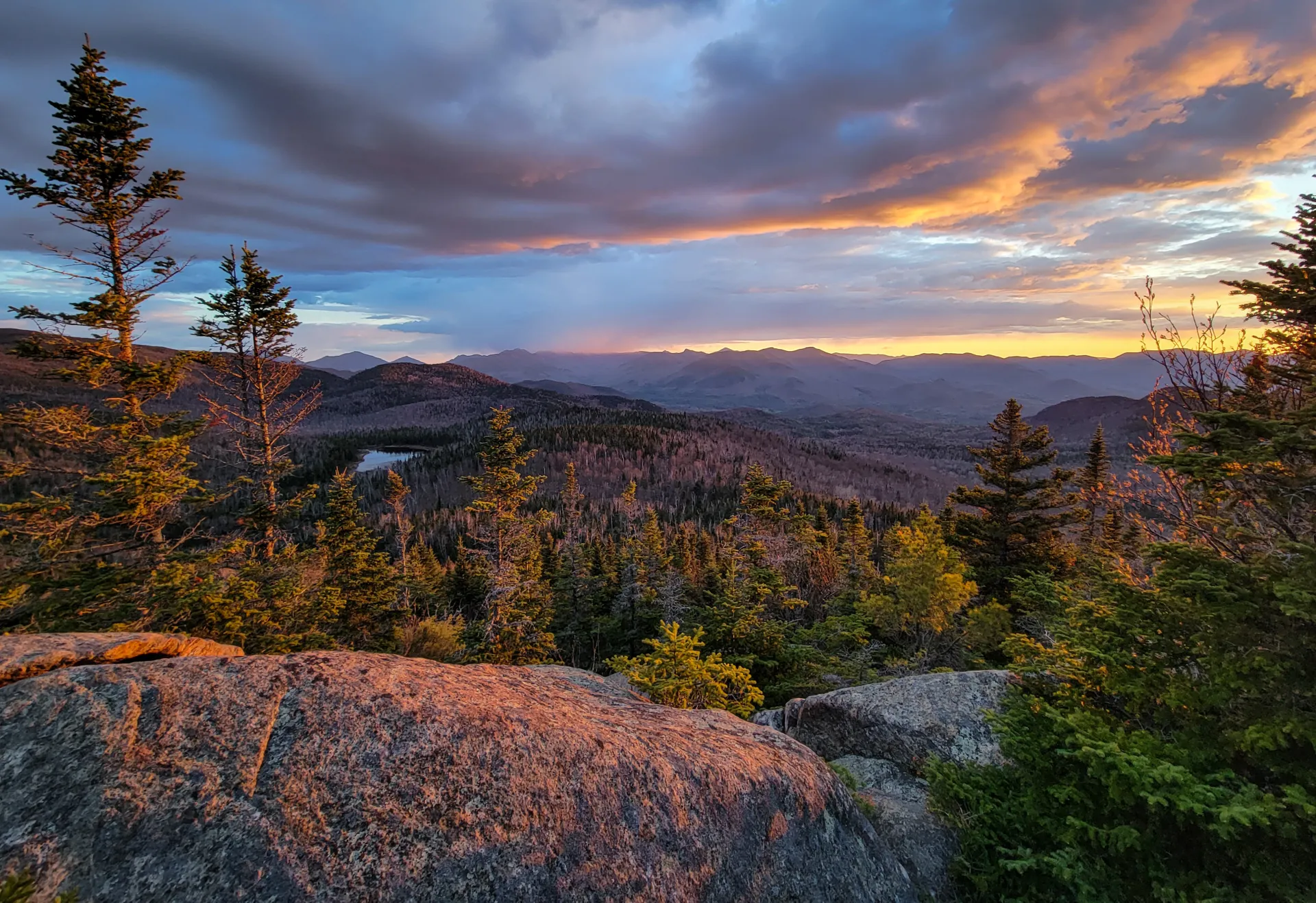 A mountainous view with a small pond at sunset