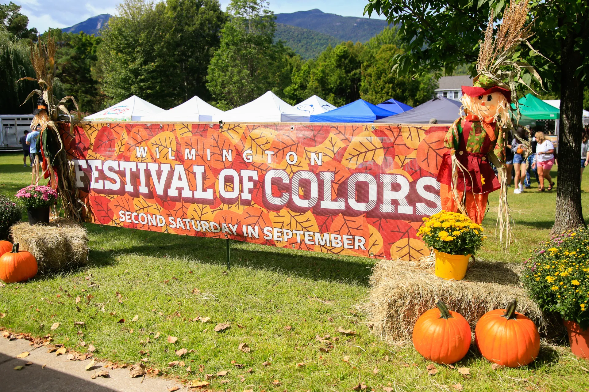 Large horizontal Festival of Colors banner in front of event bookended by hay bales, mums, pumpkins, and scarecrows