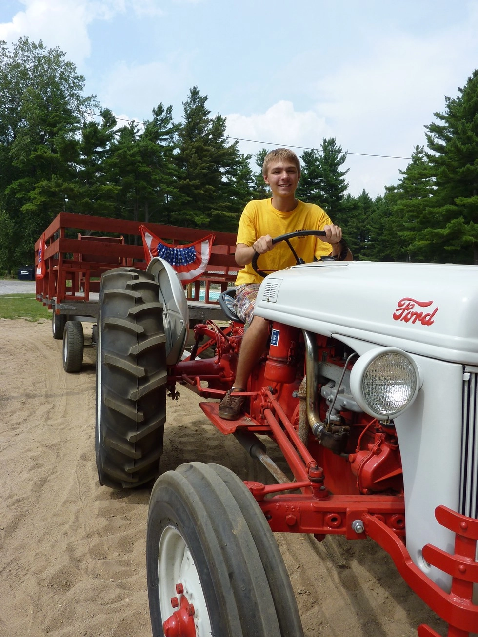 A young man on a tractor pulling a red trailer.