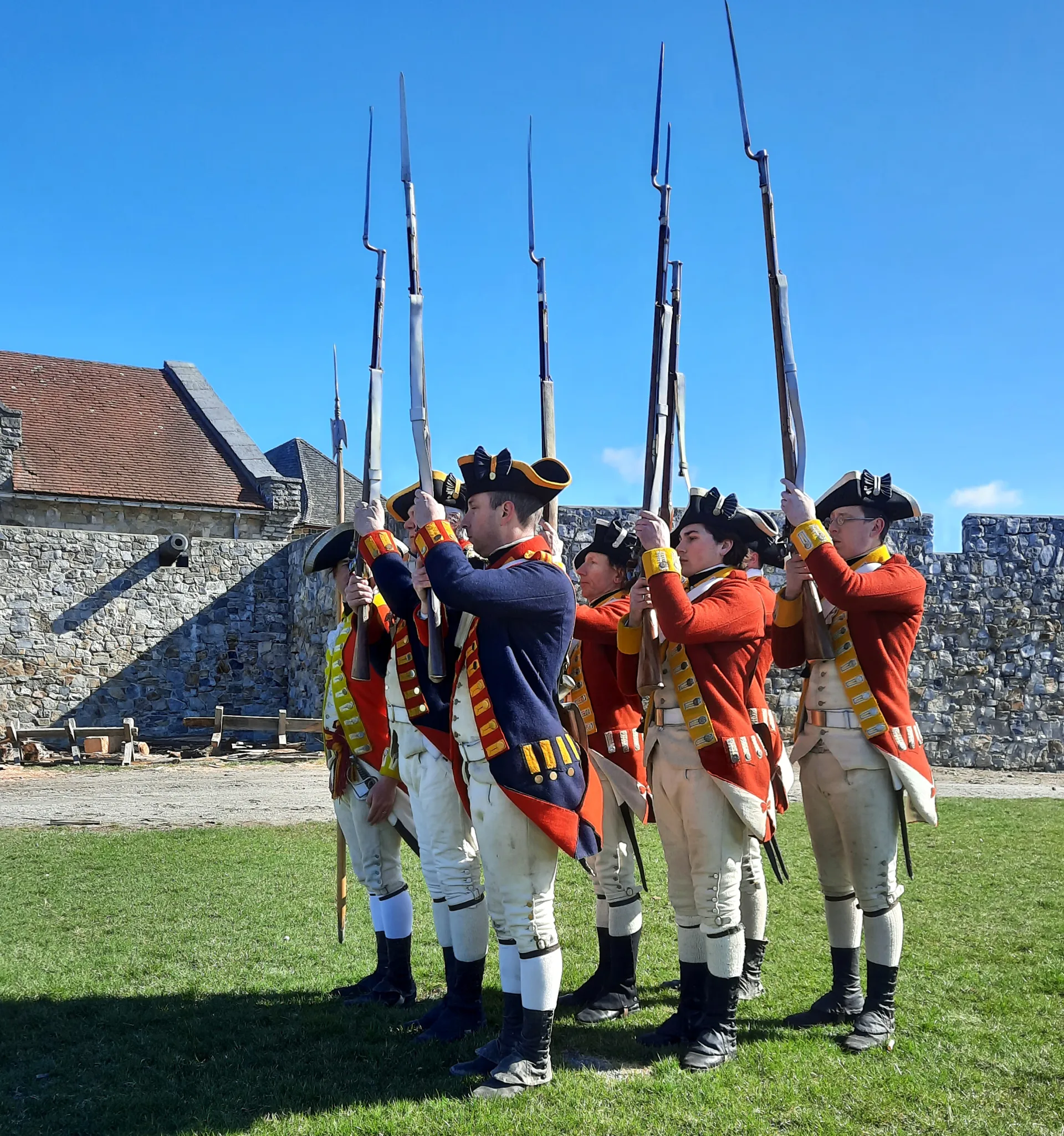 Reenactment performers stand in military formation holding their muskets with bayonets in the air