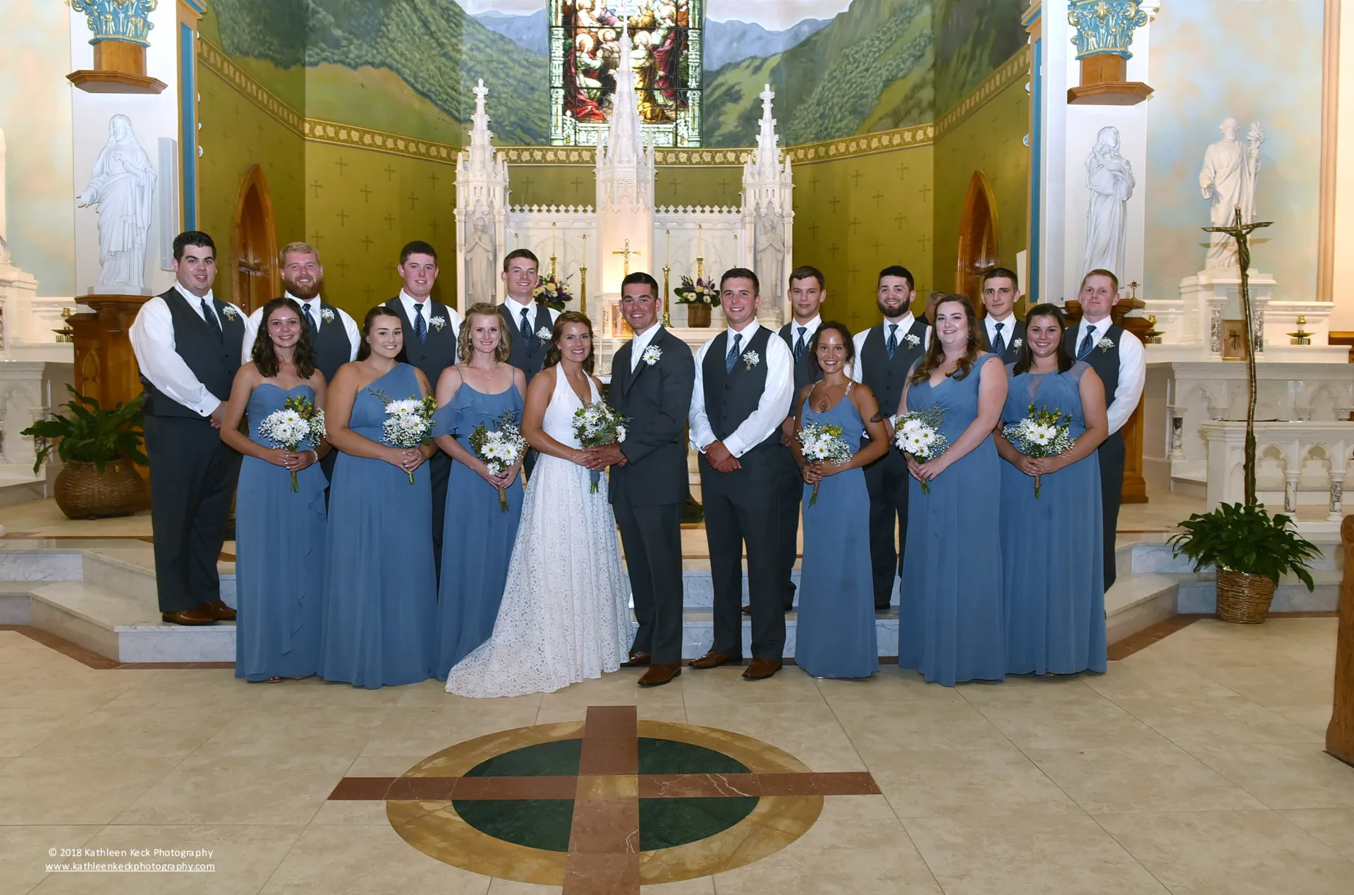 A bride and groom stand at the church alter with a sea of blue dresses of the bridesmaids.