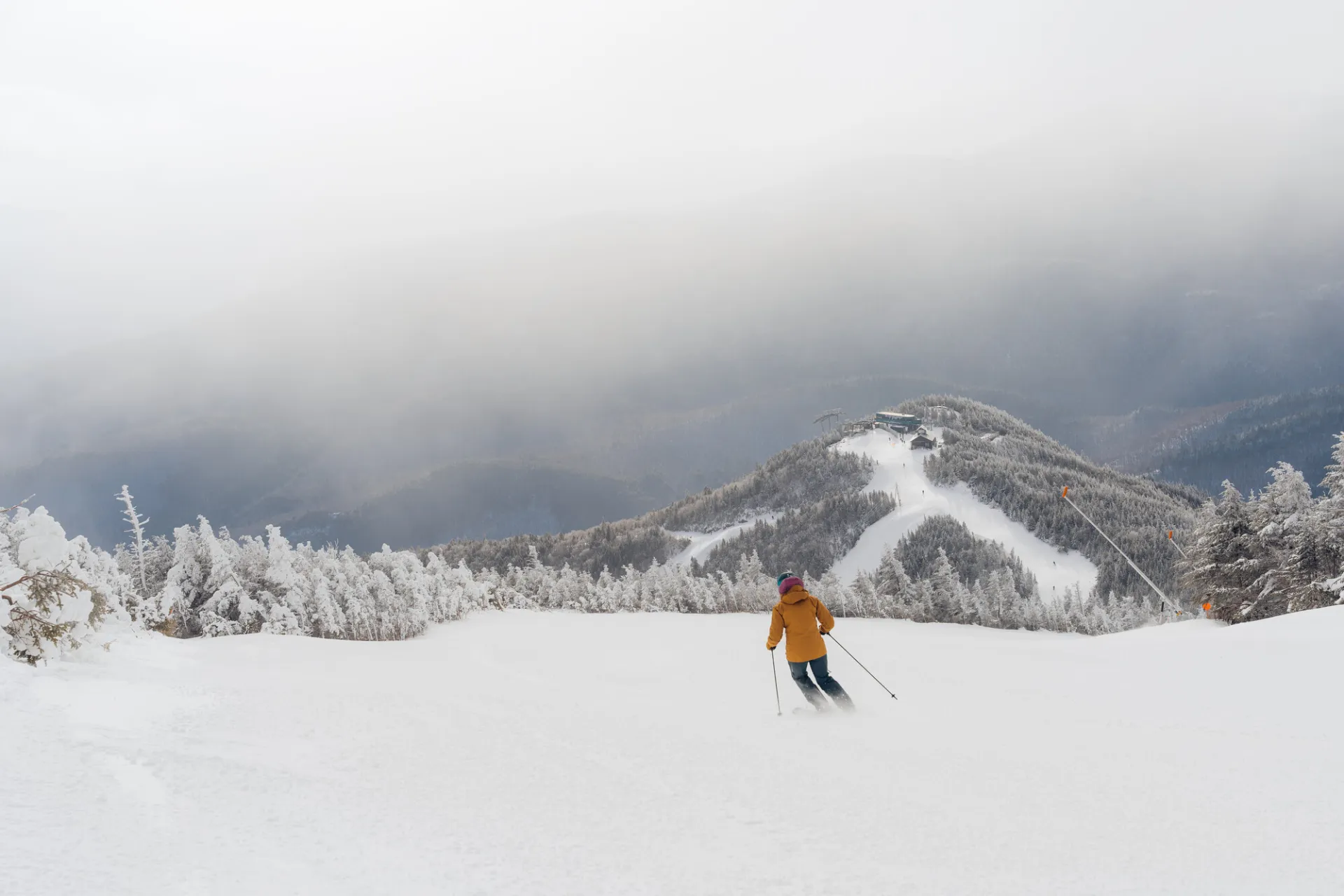 A skier in an orange jacket carves down a wide, snow-covered slope at Whiteface Mountain.