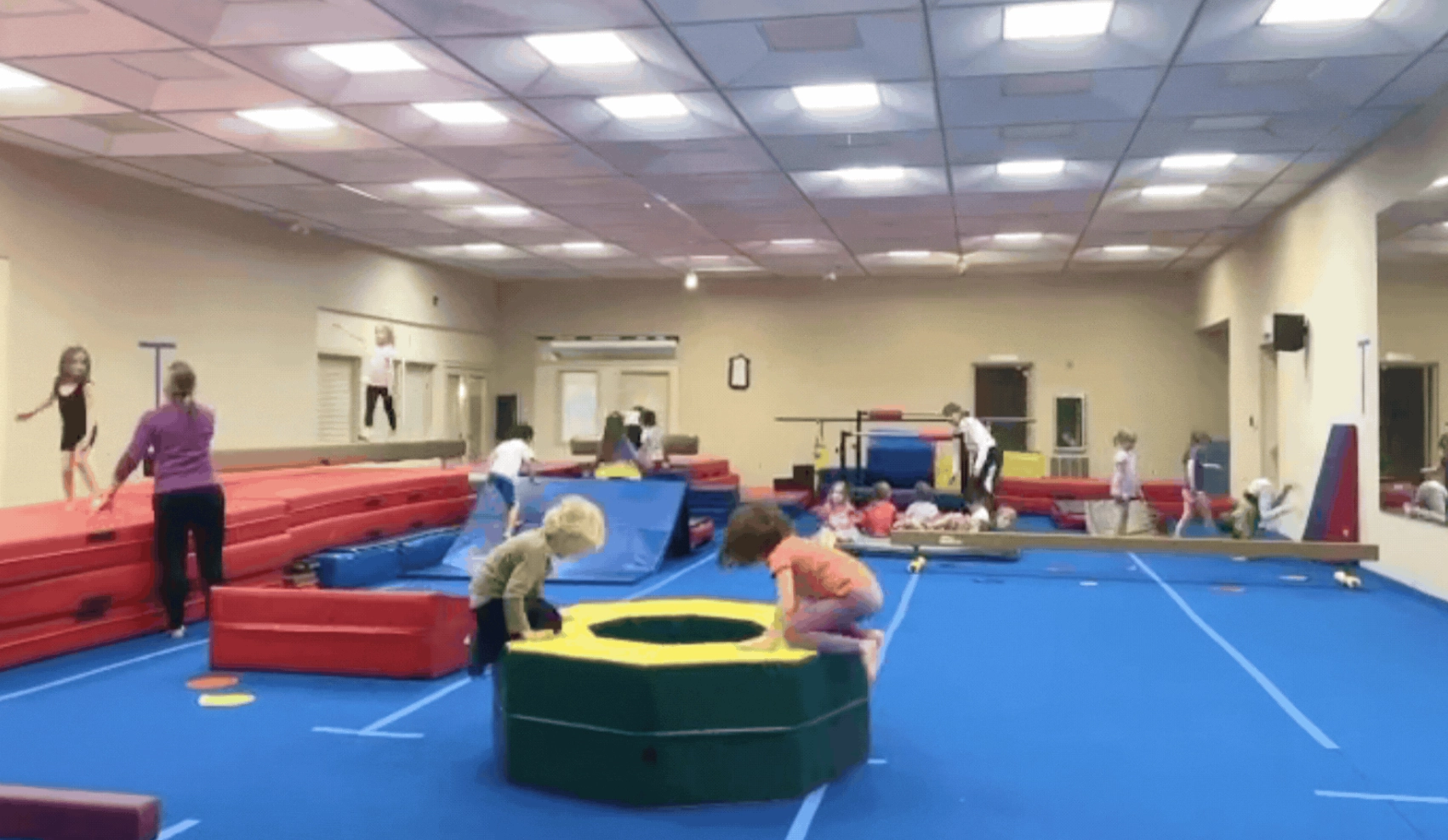 In a room full of gymnastics mats and equipment, children of varying ages practicing tumbling skills