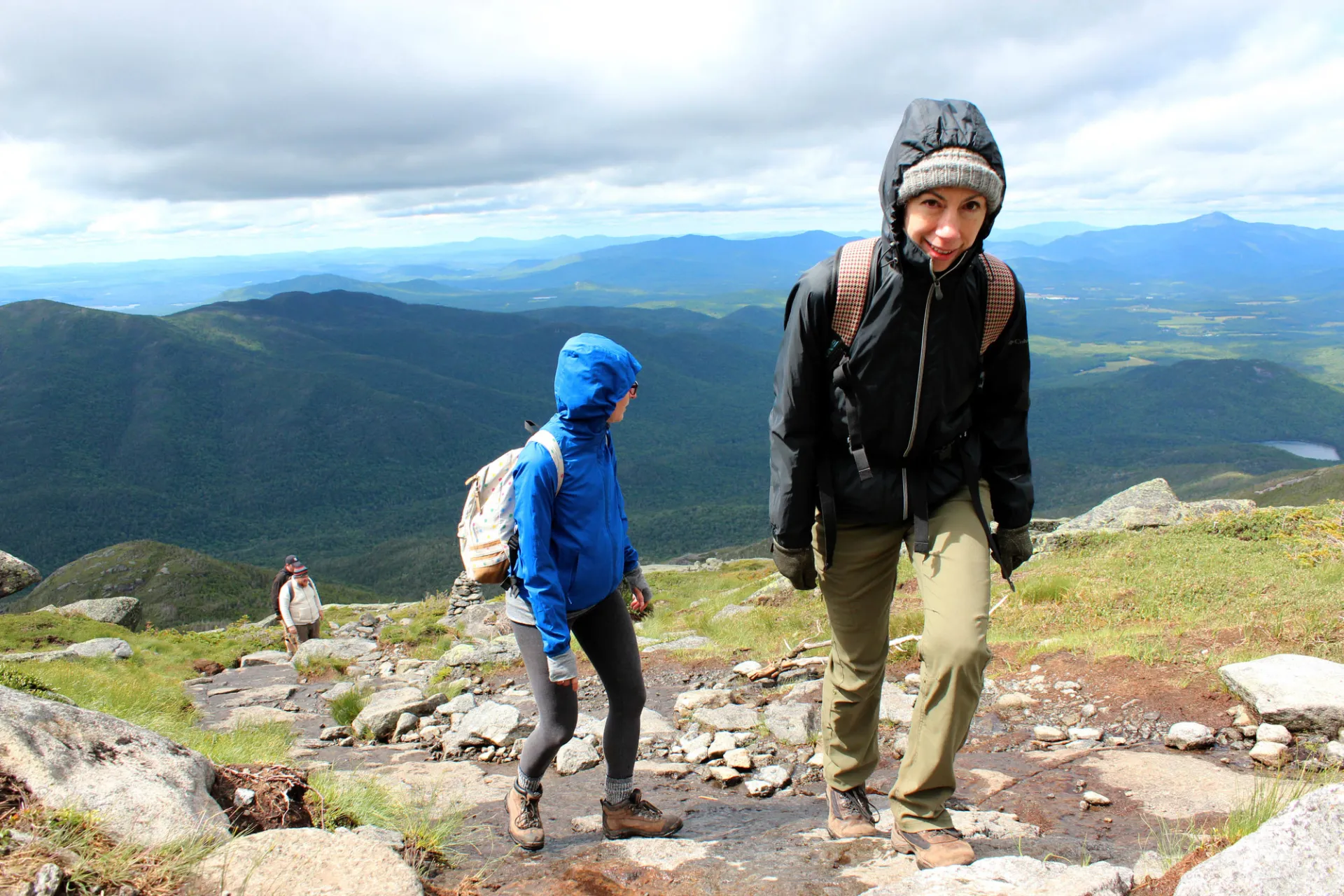 Four hikers climb a mountain with the high peaks in the background