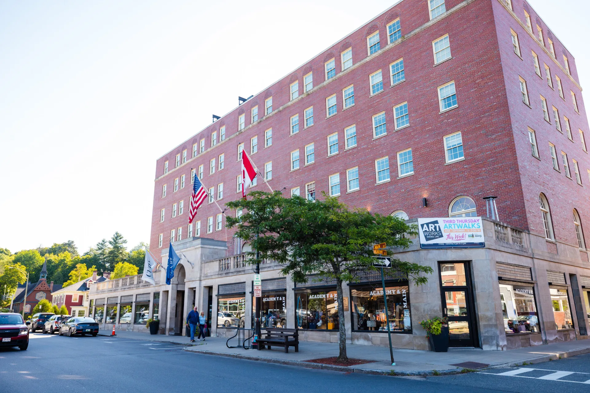 The exterior of Hotel Saranac, featuring an American flag and a Canadian flag flying near its stone-arched entrance.