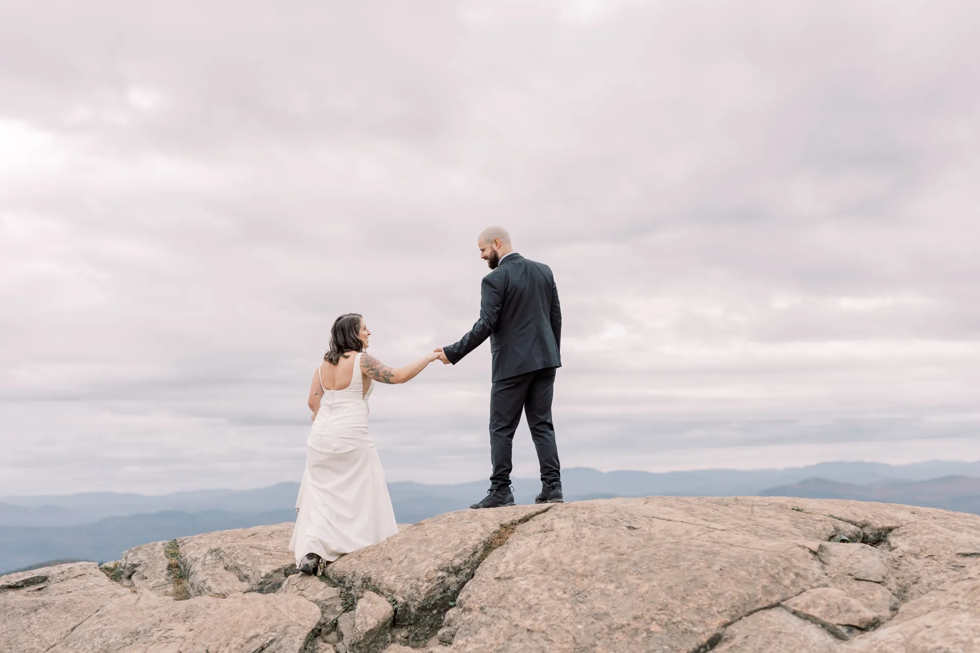 Bride and groom laugh atop a rocky knoll 