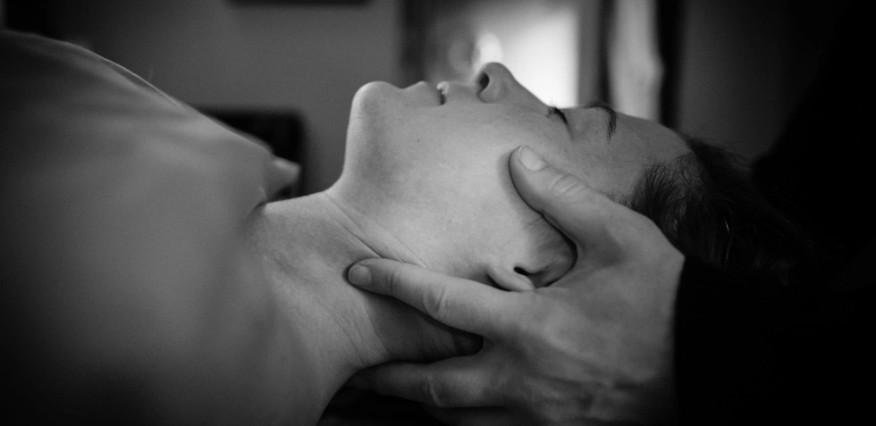 A black and white image of a massage client laying on their back while a therapist works on their spine at Healing Elements.