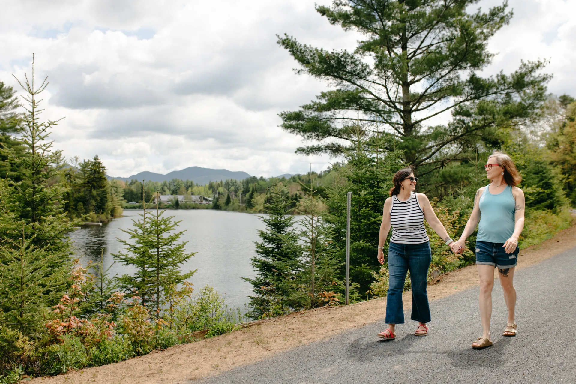 A couple holds hands while walking on a lakeside path.