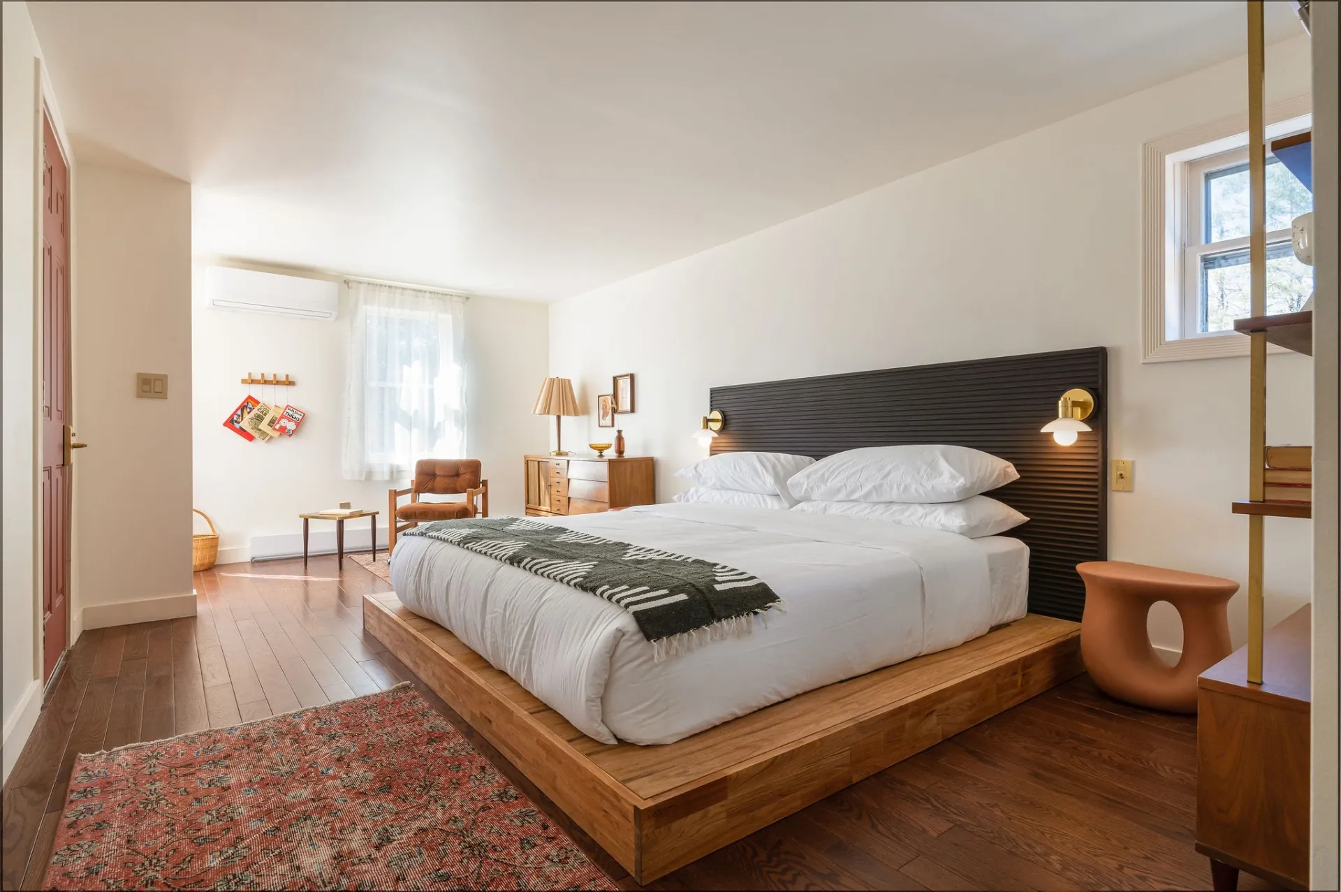 A wooden platform bed with lush linen coverings, brass sconces and organically shaped terra cotta colored nightstand