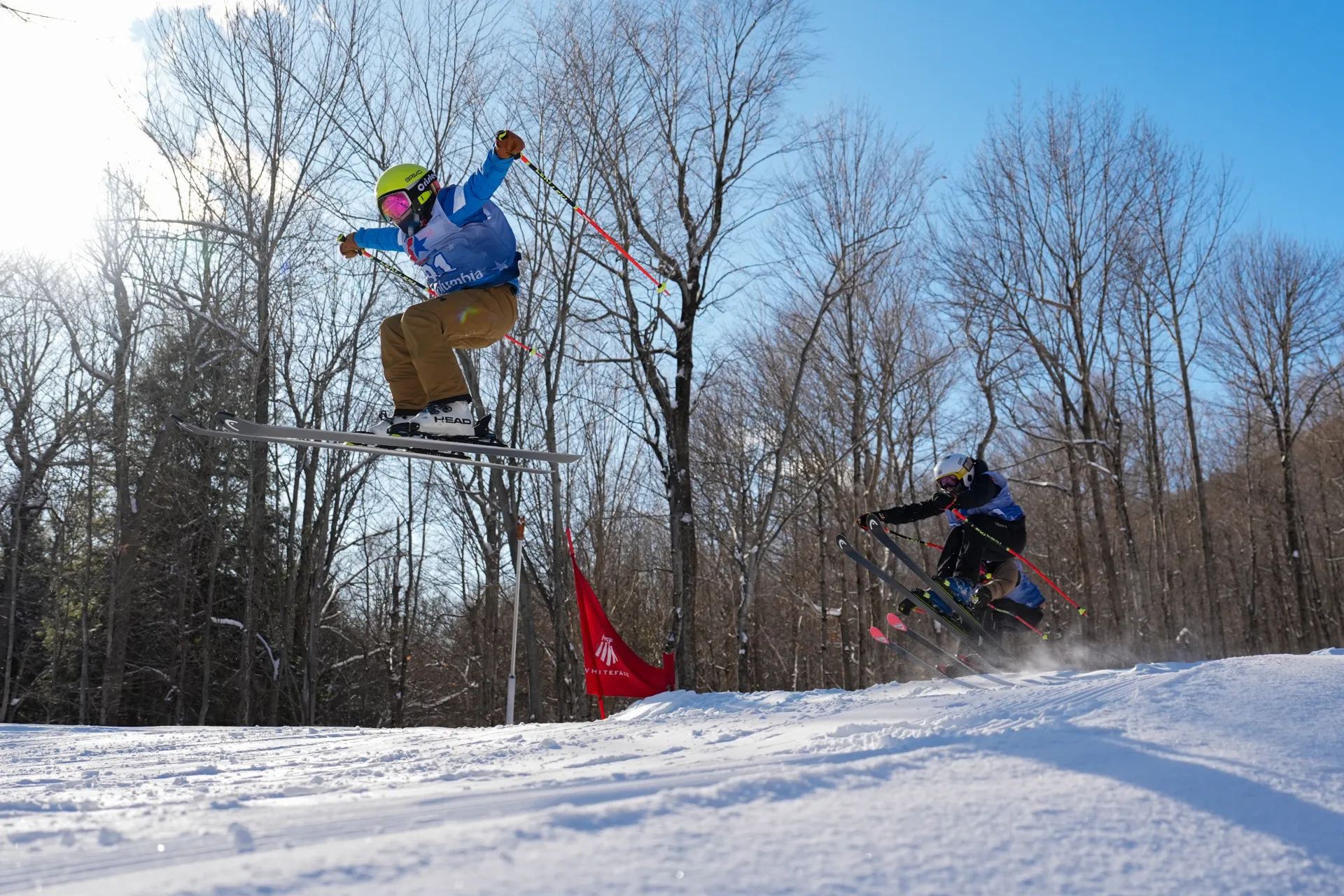 Three skiers wearing competition bibs catch air simultaneously during a cross race at Whiteface Mountain.