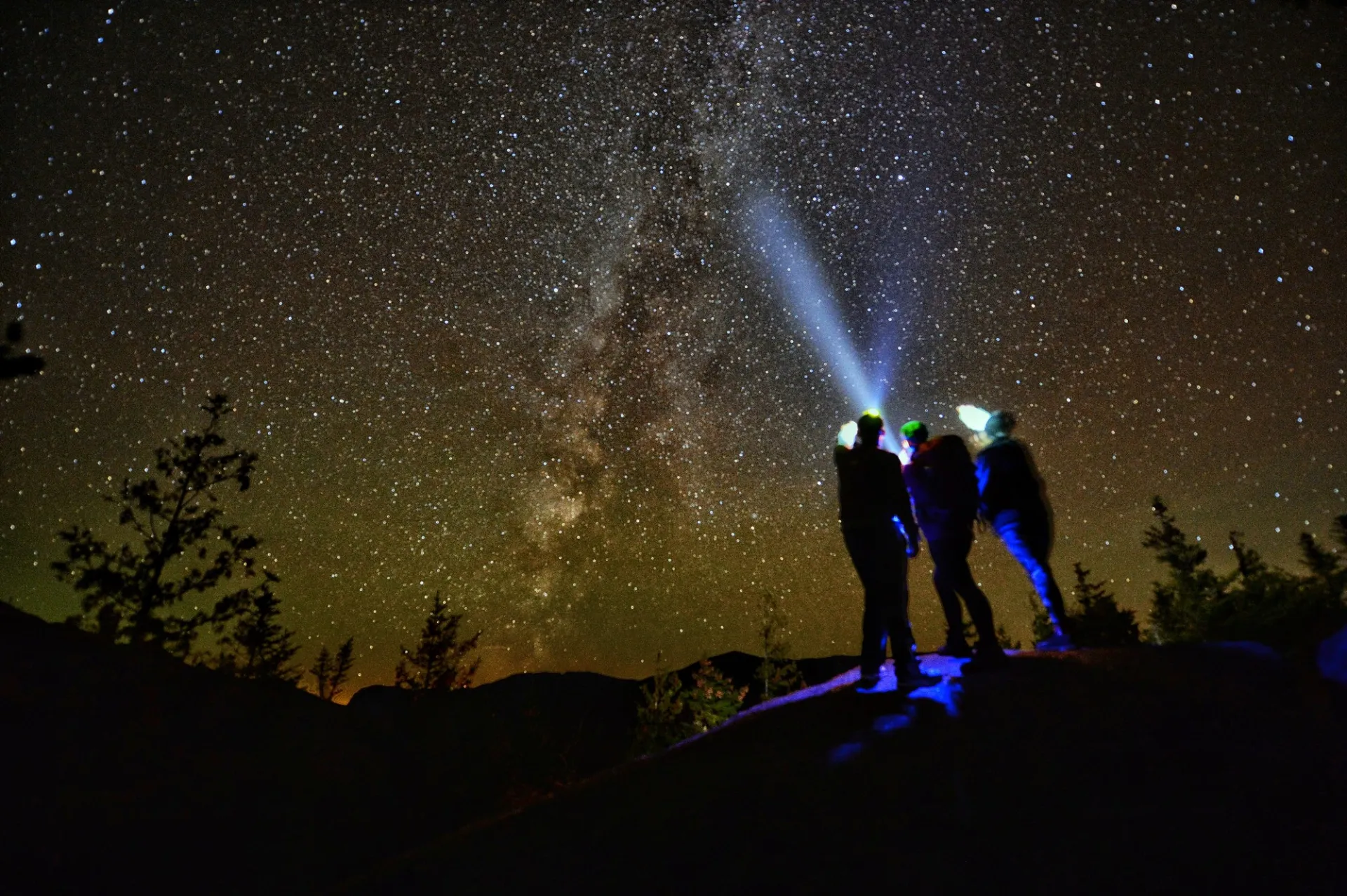 Three hikers stargazing at a summit.