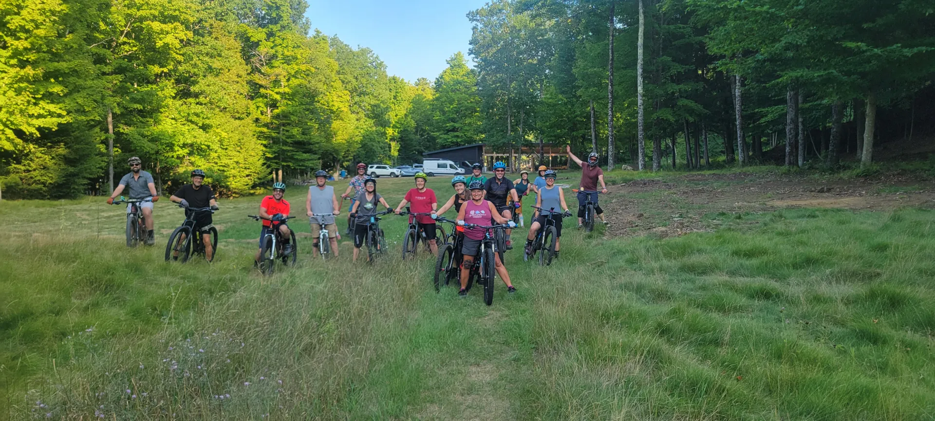Group of mountain bikers posing together on mountain bikes on lawn surrounded by trees