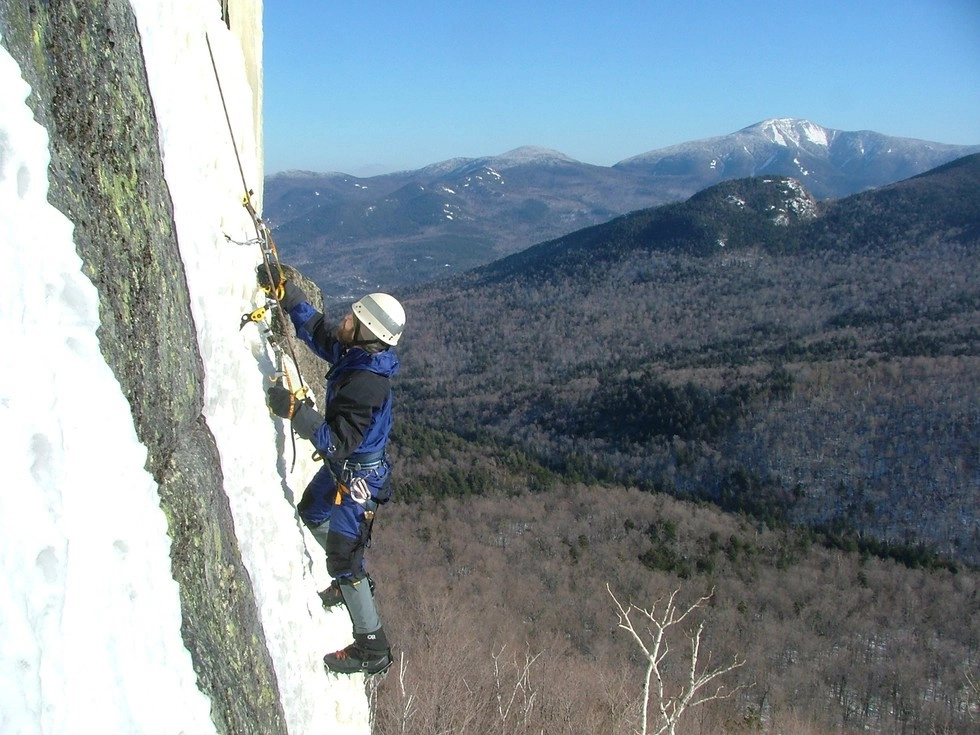 Climbing ice on the side of a cliff with mountains surrounding.