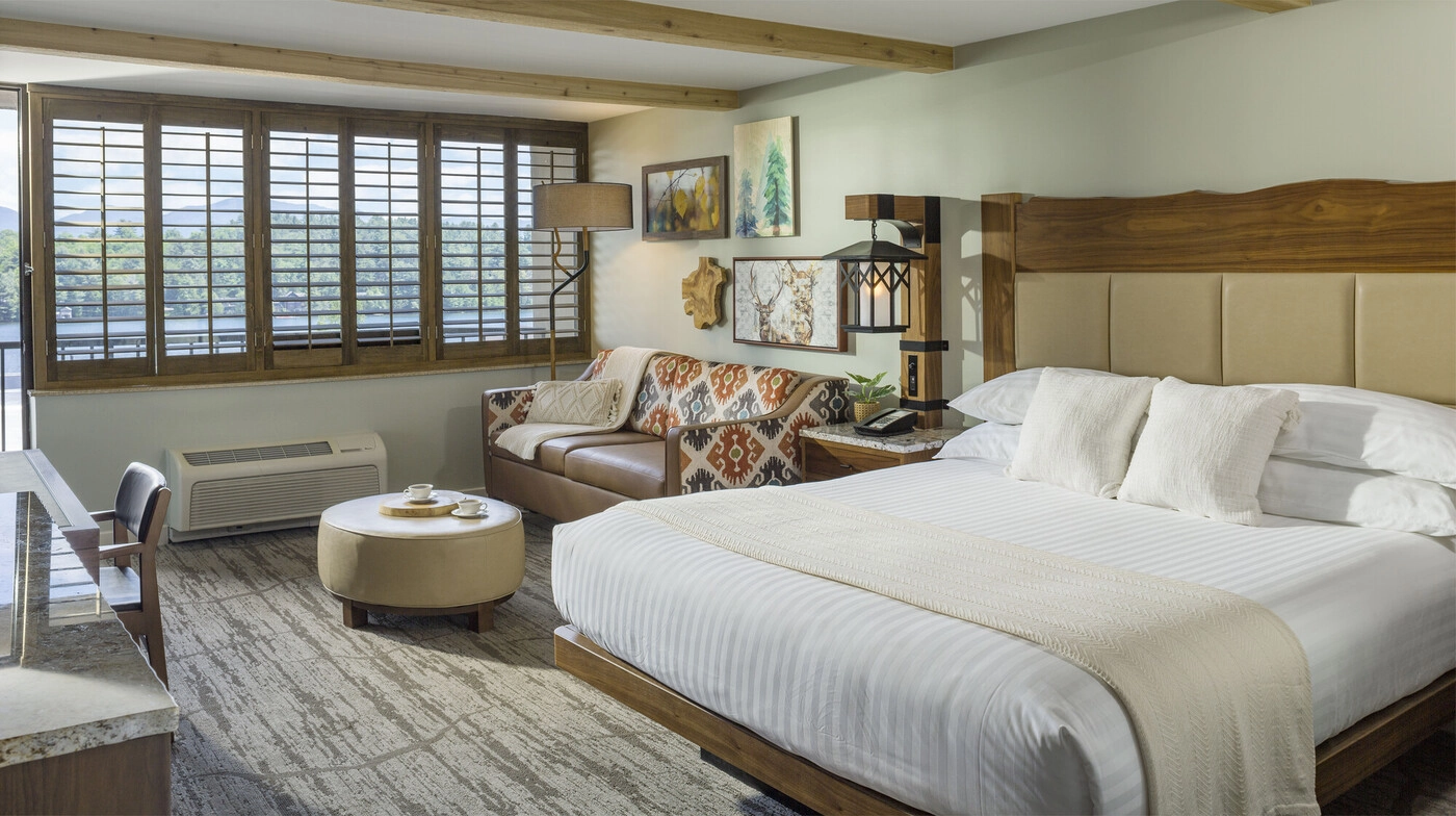 Large bed next to sitting area next to window with wooden blinds