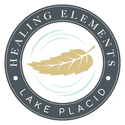 A round badge logo with a gently falling leaf in the center with the text 'Healing Elements Lake Placid".