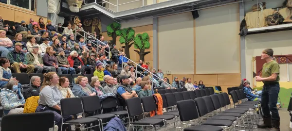 A large group of people are seated in a lecture hall listening to a speaker during the Backcountry Film Festival.