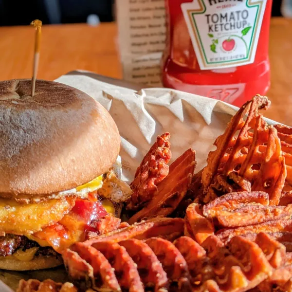 A cheeseburger topped with a fried egg and crispy bacon with golden waffle cut fries.