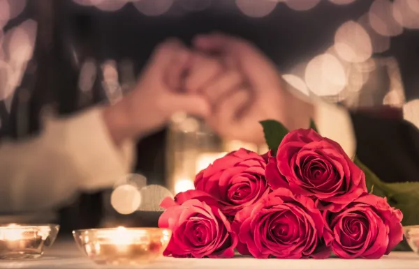 Bunch of roses on candlelit table with people holding hands