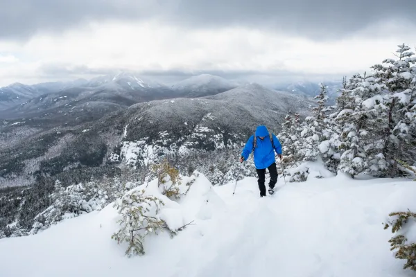 A man in a blue coat walks up a snowy mountain trail