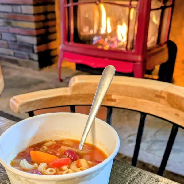 A cup of rich soup next to the red gas fireplace