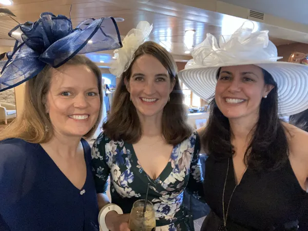 Three women in Kentucky Derby dress and hats smile together for the camera