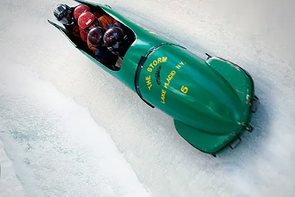 A group of five riding a green bobsled on an icy track.