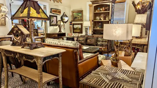 A view of the show room at L Post Rustics featuring many styles of log furniture from end table to couches, table lamps, sconces and tall hutches flanked by wall decor.
