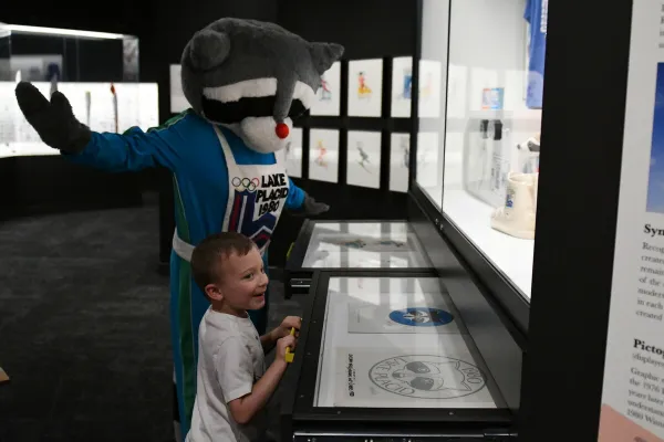 Young boy looks at Olympic Museum display with Roni the Raccoon mascot