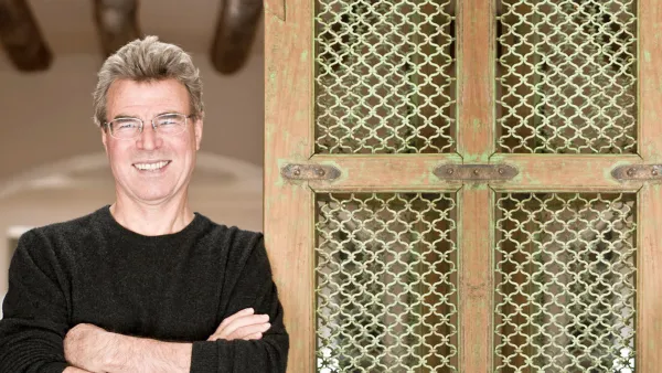 Steve Thomas smiles next to a decorative, green-painted wooden screen with a patterned metal grille.