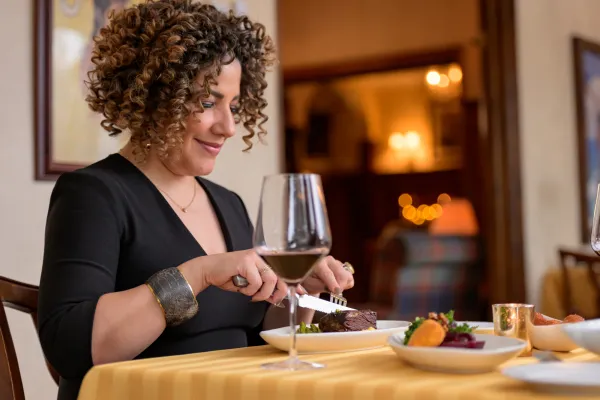 A woman at the Interlaken Inn Restaurant cuts her meal with a glass of wine and warm glow from the fireplace