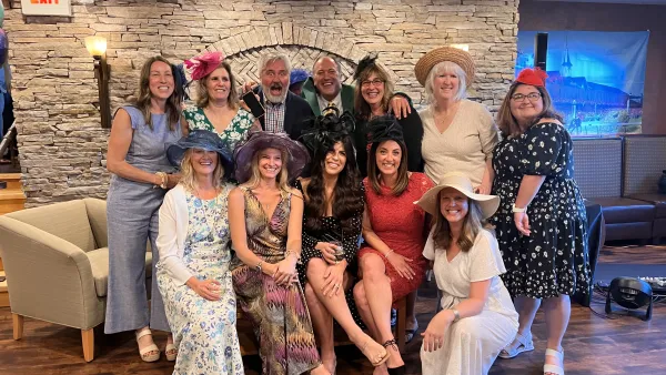 Large group of people in Derby dress pose for group photo in front of stone wall in restaurant