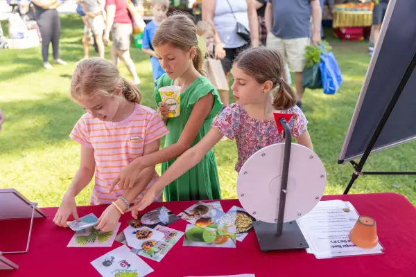 Three girls at a table with a prize wheel, looking at pictures of food and other items.