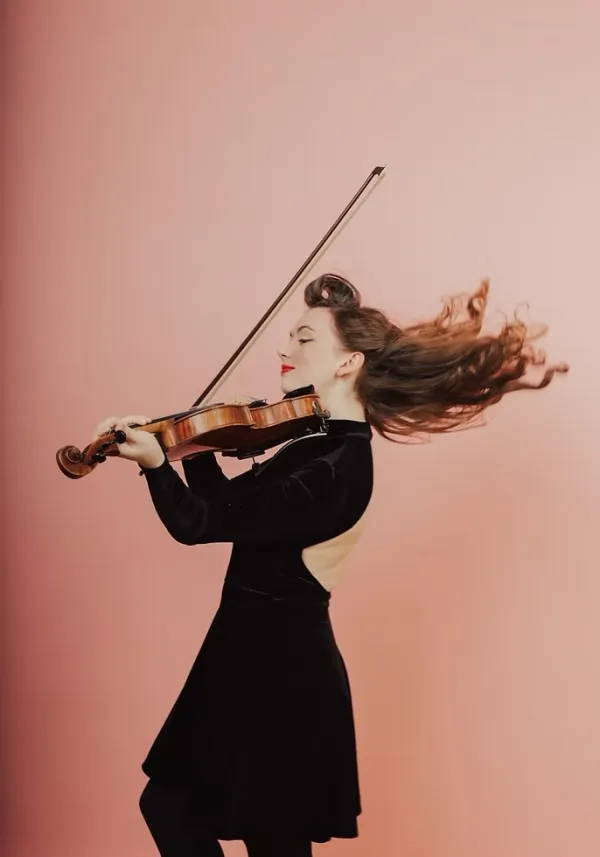 Kathleen Parks in black velvet dress plays fiddle in front of pink background