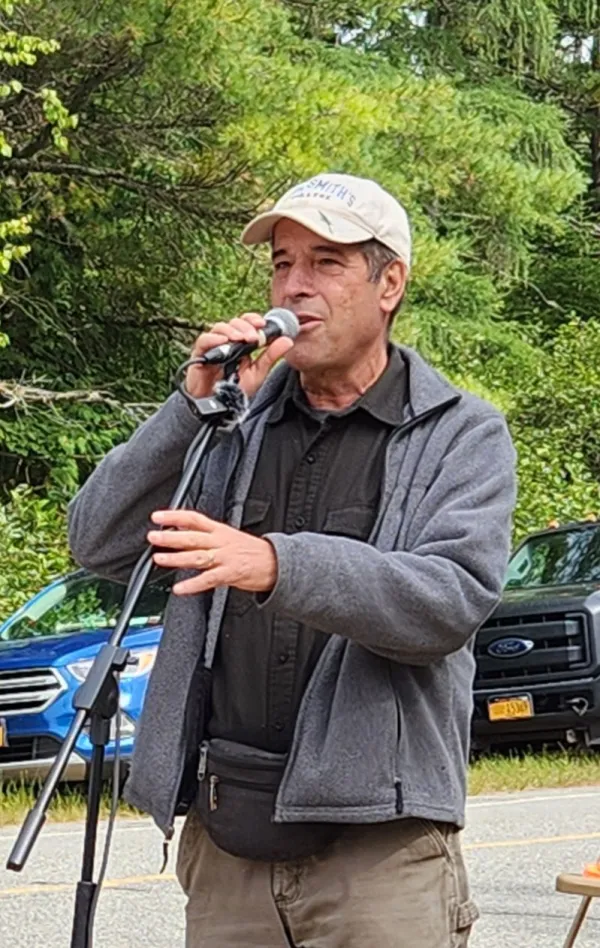 Curt Stager speaks into a microphone wearing a grey jacket and baseball cap
