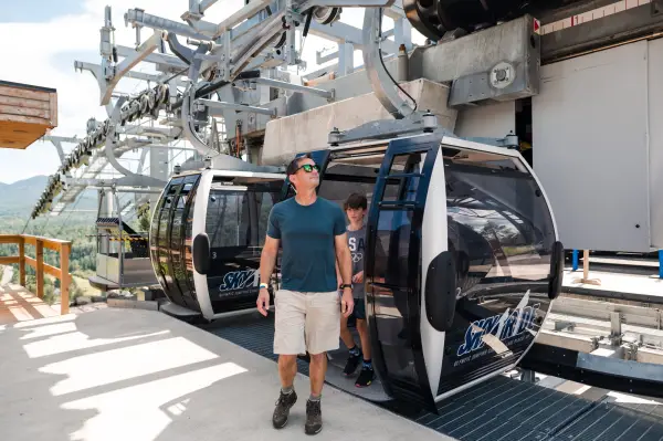 Man steps out of gondola looking around wearing t-shirt, shorts, and sunglasses