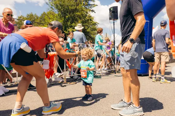 Race worker hands medal to small smiling child at finish line of Lake Placid Ironkids race