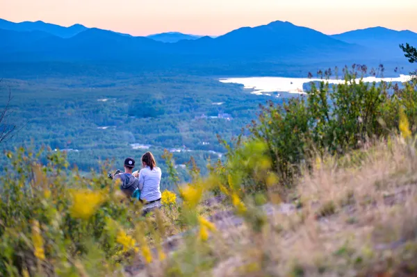 A couple stares out at the silhouette of the high peaks in the Adirondacks from the summit of Haystack Mountain during sunsetHaystack Mountain