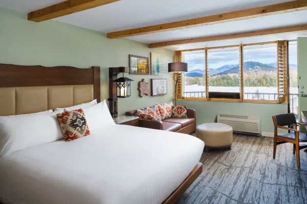 Large bed in hotel room next to leather couch with ottoman and winter lake view out the window