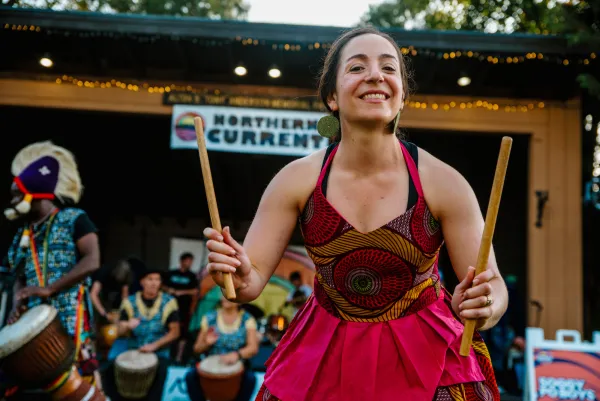 A friendly drummer in a colorful dress smiles into the crowd