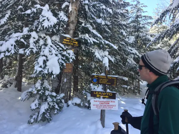 A hiker looking at wooden trail signs in the winter