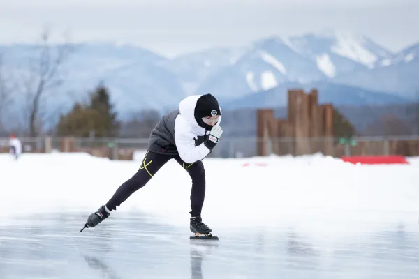 A speed skater in motion with the high, snowcapped mountains in the background.