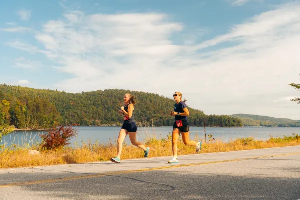 Two women run along a paved road during the Adirondack Marathon.