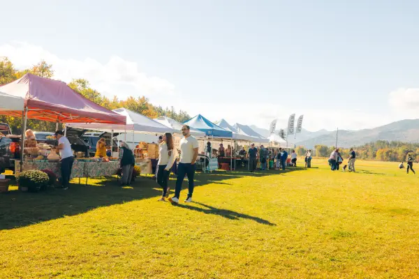 Couple holding hands walks past row of farmers market tents