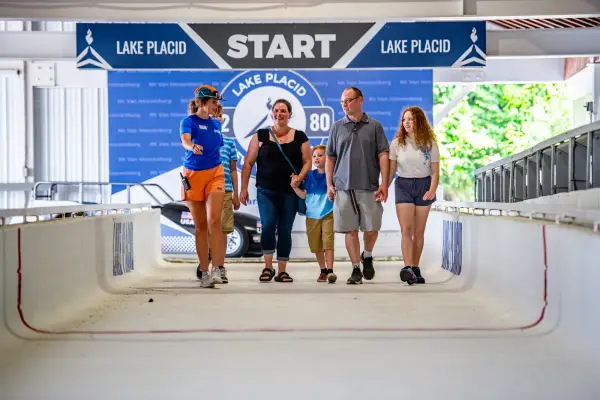 Mother, father, daughter, and two sons follow tour guide at start line of Mt Van Hoevenberg bobsled track