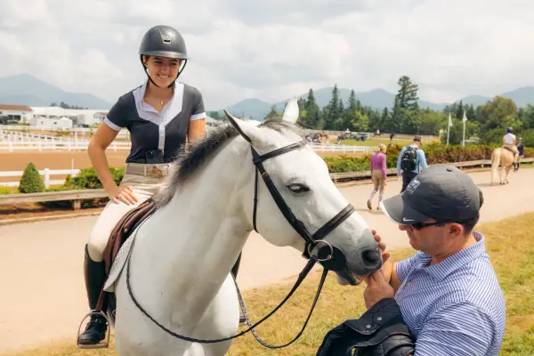 A rider, her horse, and person petting her horse.