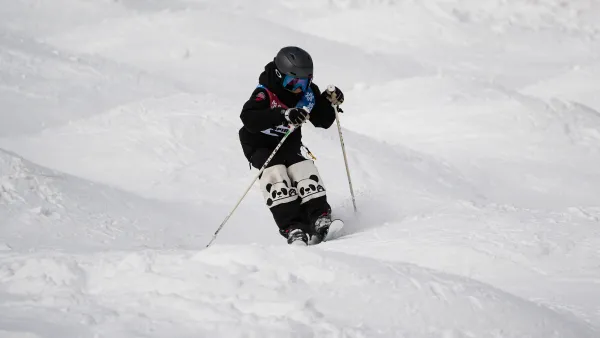 A skier wearing black gear and panda-patterned knee pads navigates a mogul field on a snowy slope.